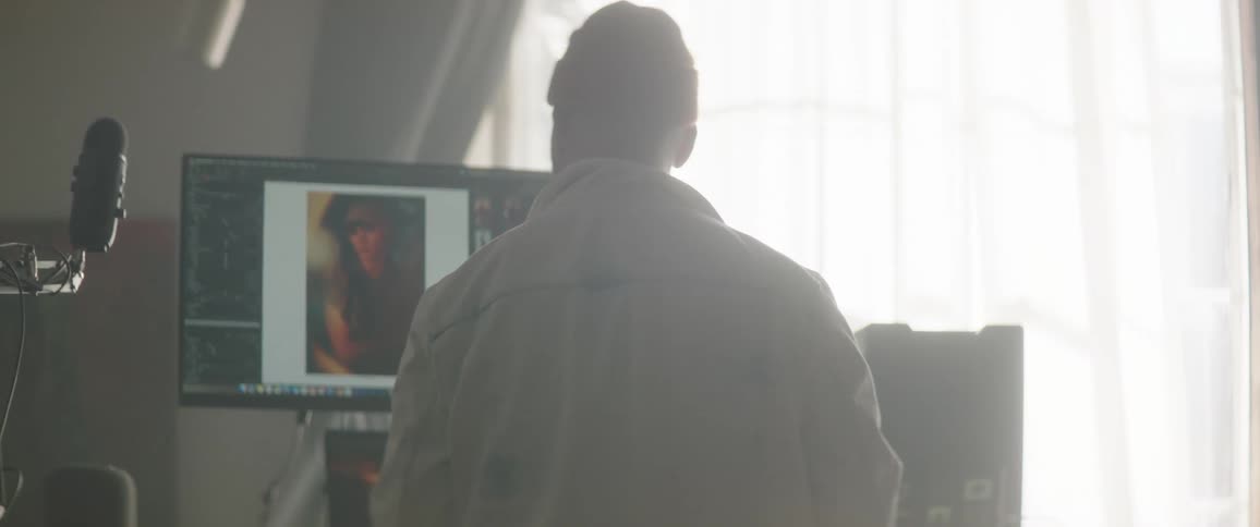 Man wearing a toque walks over to a table holding several computer monitors and a computer