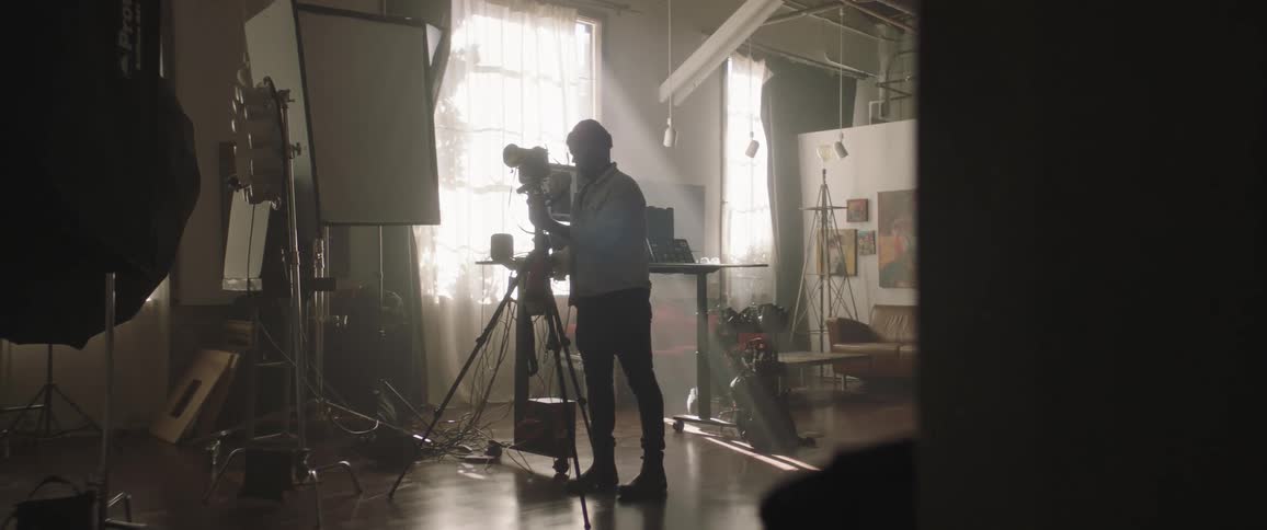A man with a hat in a studio adjusting a camera on a tripod