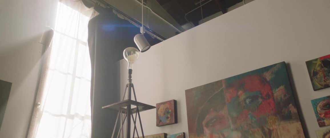 The sun lights an art studio with multiple paintings on the walls