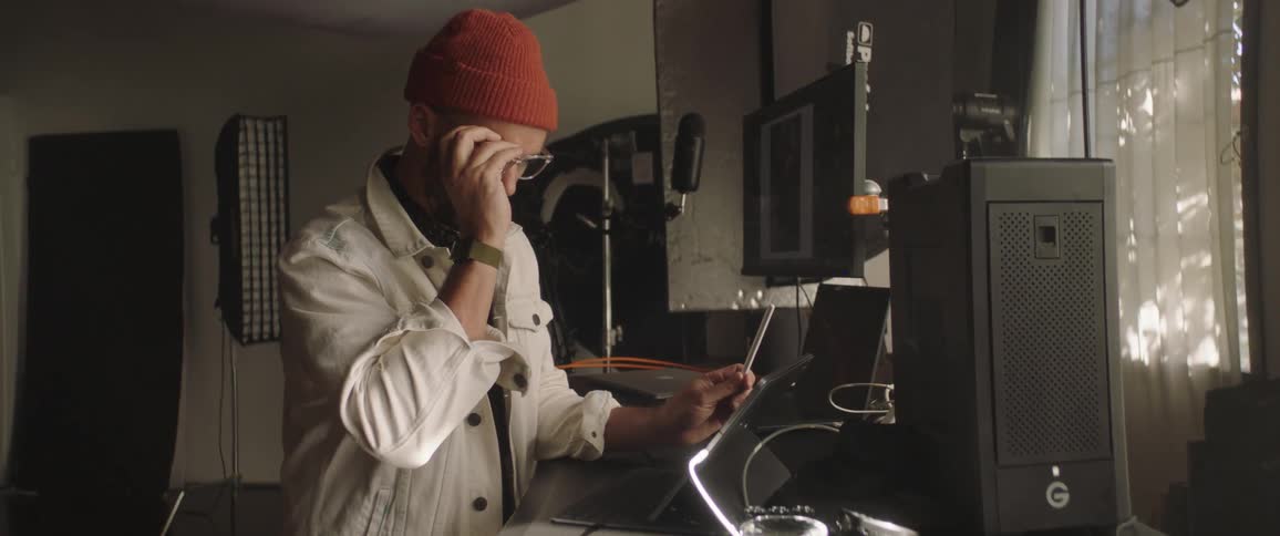A man puts on his glasses to get a closer look at his tablet while at a standing desk in a photography studio