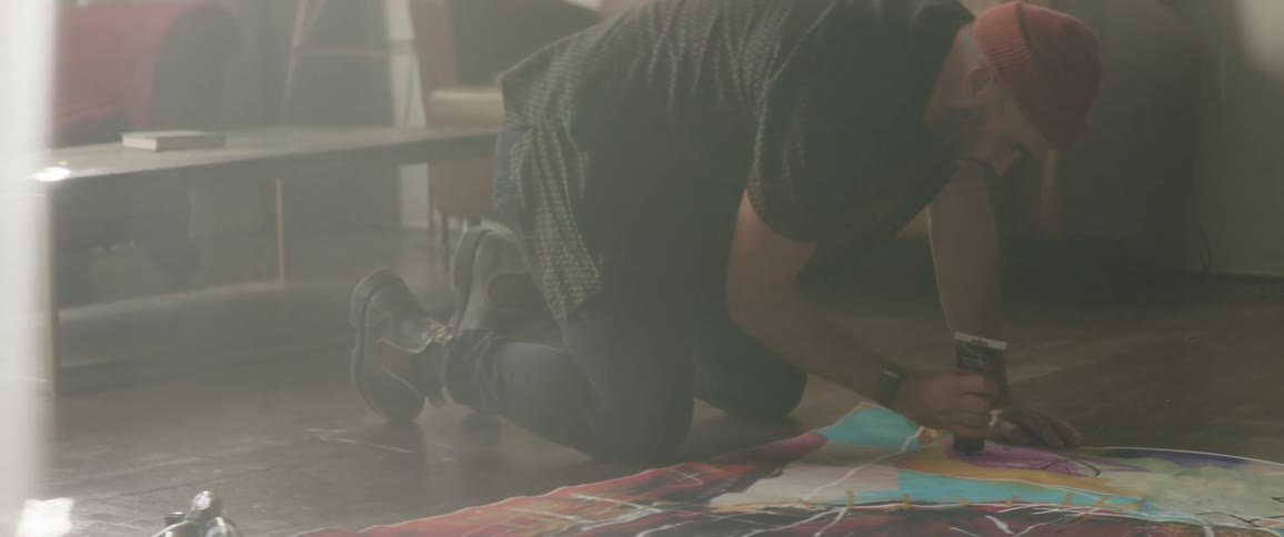 Artist kneeling on the floor of the studio painting with oil over canvas