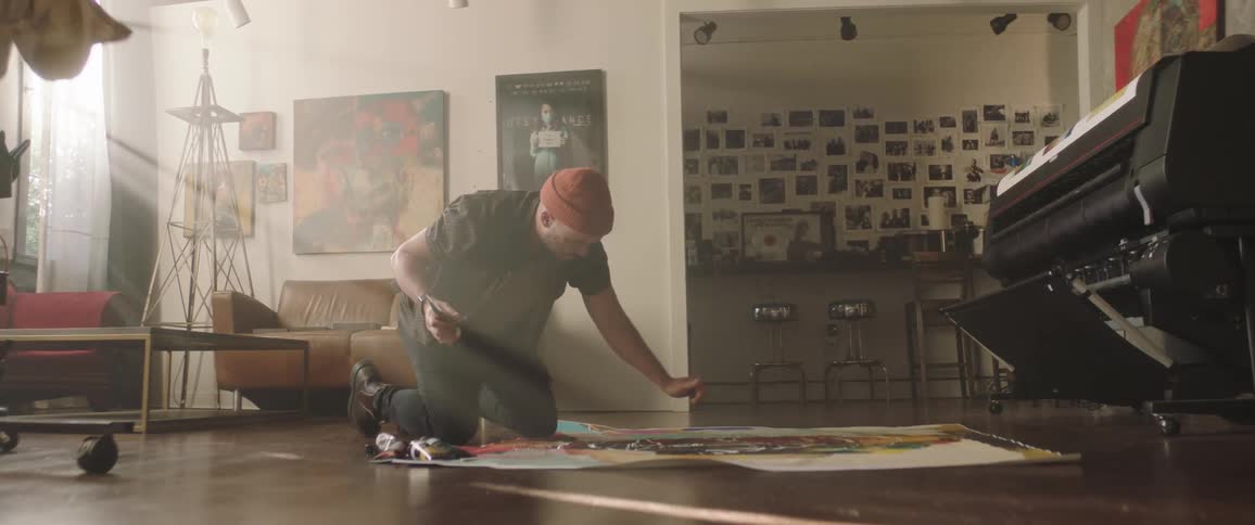 A man is painting on a canvas on his living room floor