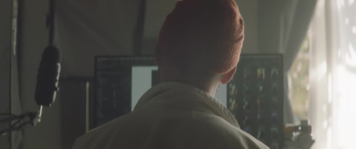 A man with a hat in a room next to a microphone and a computer screen
