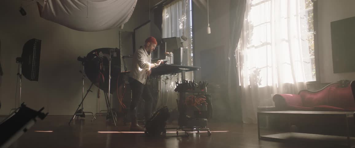 An artist stands at a table inside a studio working on a tablet
