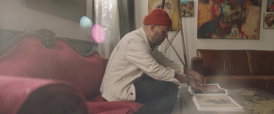 Man sitting on a red velvet couch reading a book over a coffee table