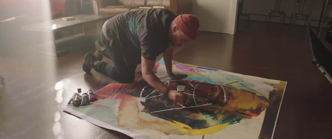 Artists painting with tubes of oil over a canvas laid on the floor
