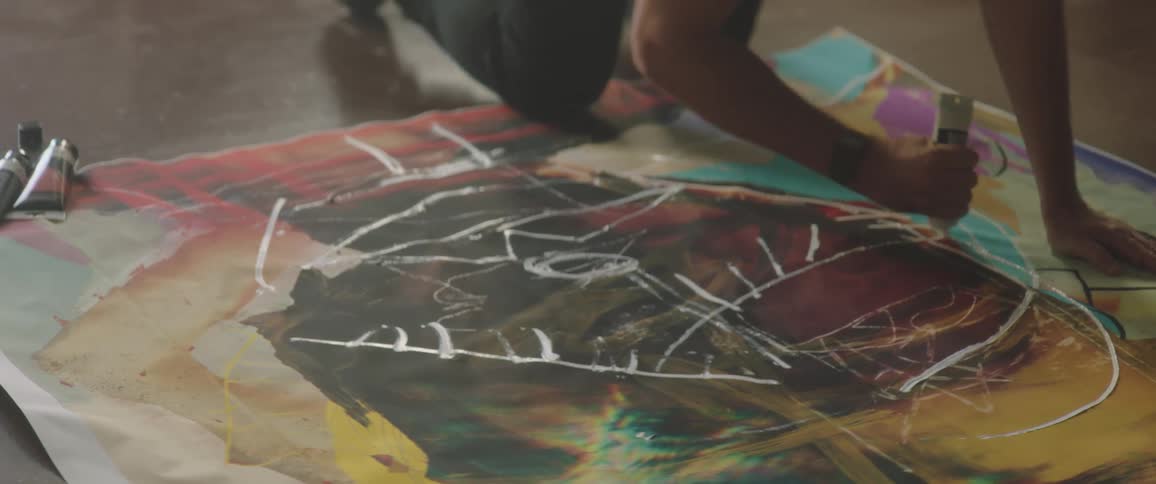 A man uses a tube of paint on a canvas on the floor