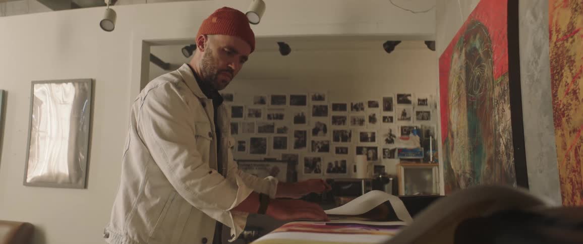A man with a hat in a room looking at a poster with a wall in the background