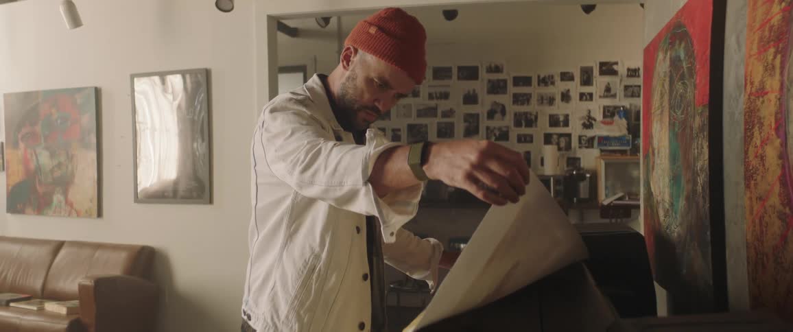 Man stands in studio examining large poster sized printouts near wall art