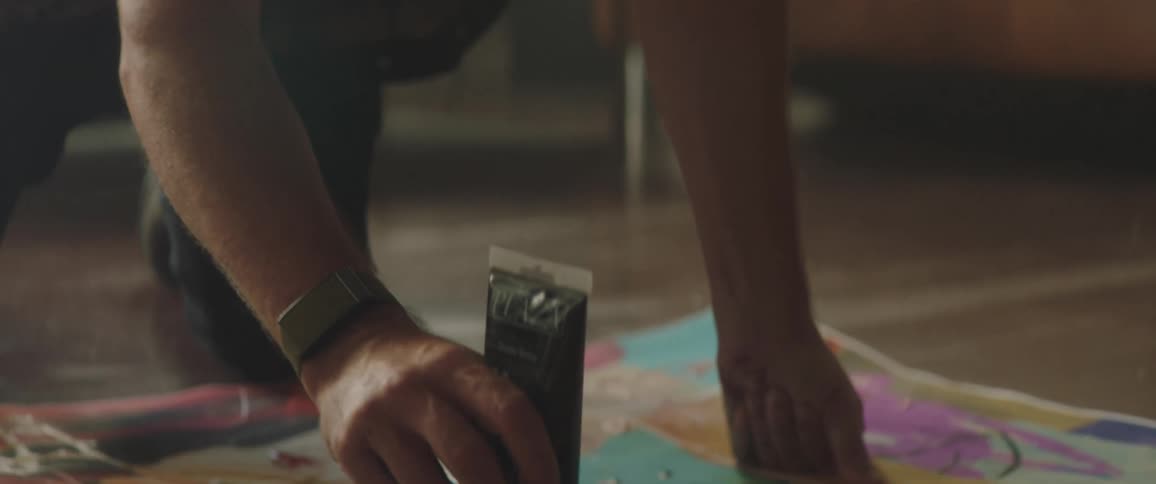 A man with a hat in a room applying paint to a canvas on the floor