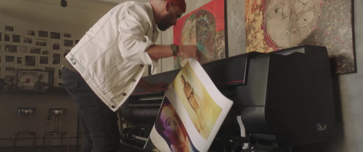 A man takes a large paper of three photos from an oversized printer
