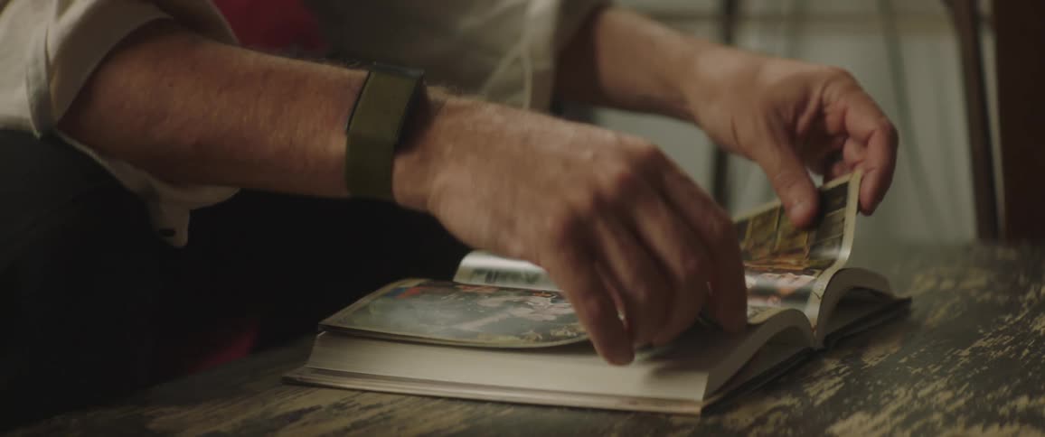 A man sitting on a sofa flipping through a small book with pictures during the day