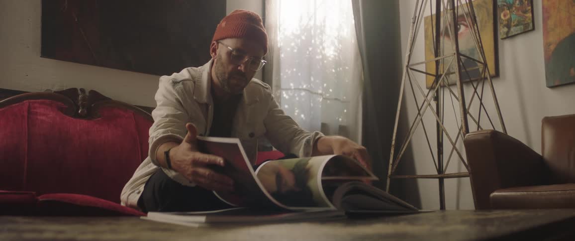 A man sitting on a sofa looking at the artwork in a coffee table book