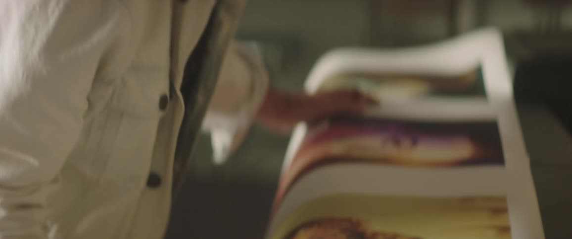 A man with a hat in a room looking at a poster with a wall in the background