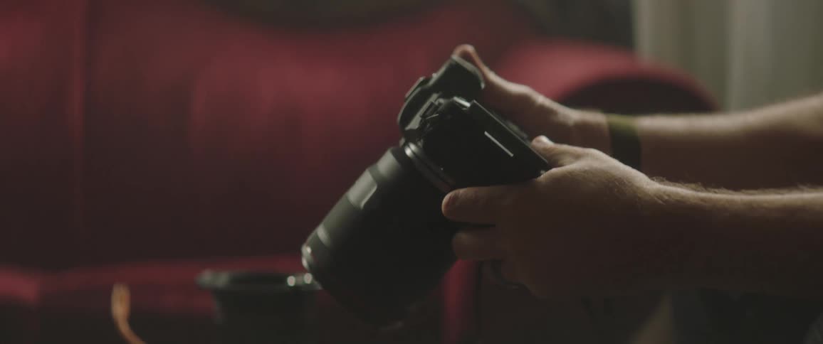 A man sitting down indoors holding a photography camera