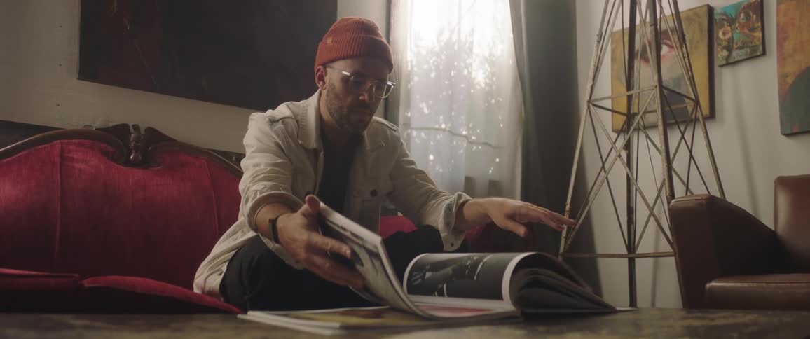 A man sits on his couch and flips through a coffee table book of black and white photographs