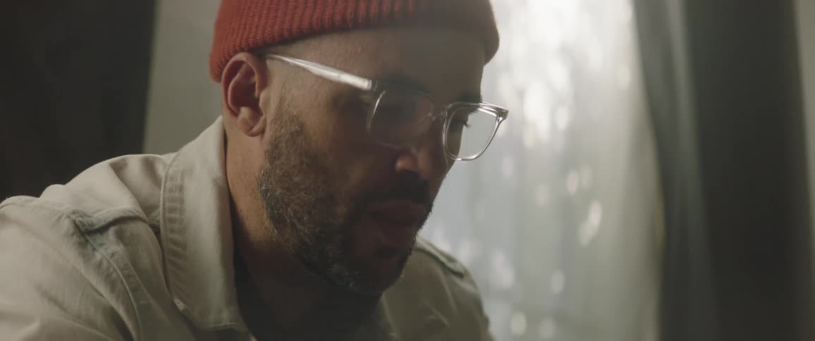 A man with a hat and glasses sitting on a couch looking through a book