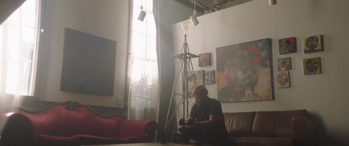 A man in a room sitting on a couch holding a camera lens with a wall in the background