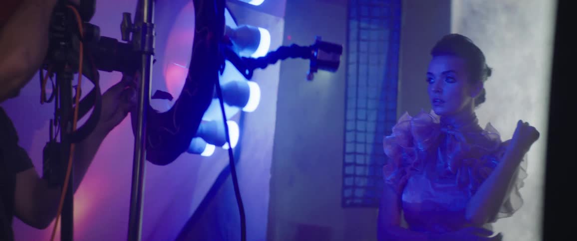 A man taking pictures of a female model at a photo shoot inside of a room glowing blue lighting