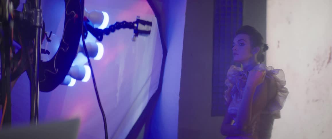 A man in a studio with a camera taking pictures of a woman with a screen in the background