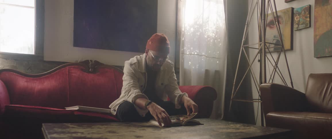 Man sitting down indoors at a couch flipping through a book on a coffee table during the day