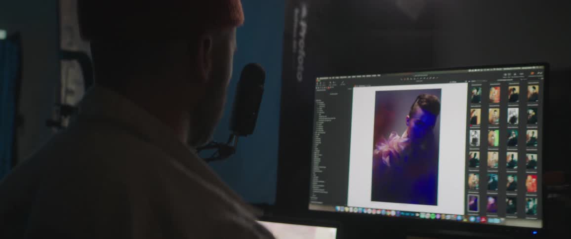 Man wearing knit cap looks through photo images of female model on monitor