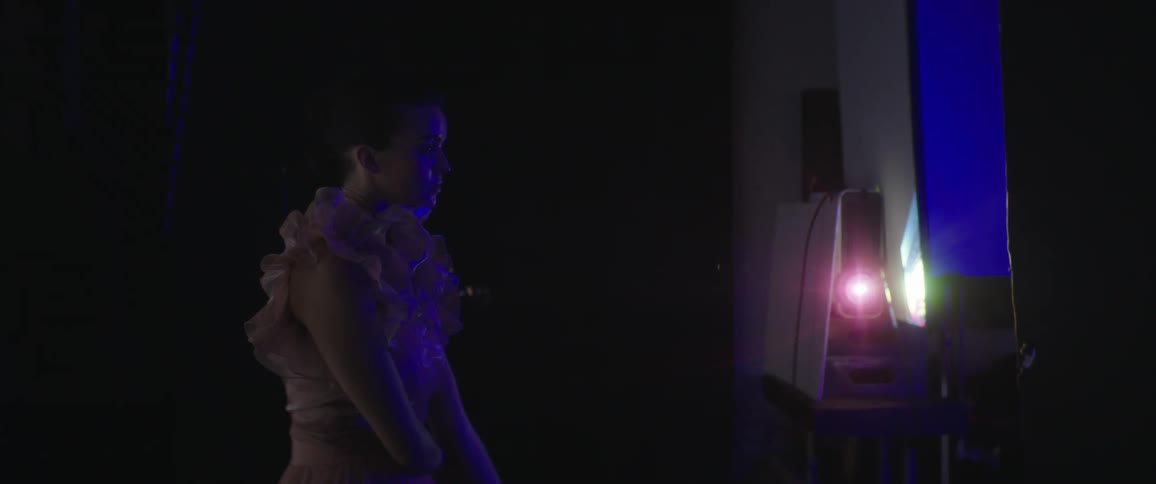 A female performer stands backstage near a blue screen and glowing light