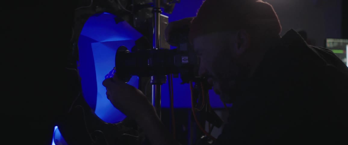 Photographer stands behind camera aiming at target under colored lights in photo studio