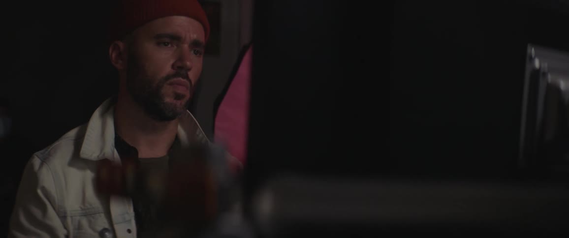 Man with a red woolly hat a beard and a white jacket works on desktop in art studio