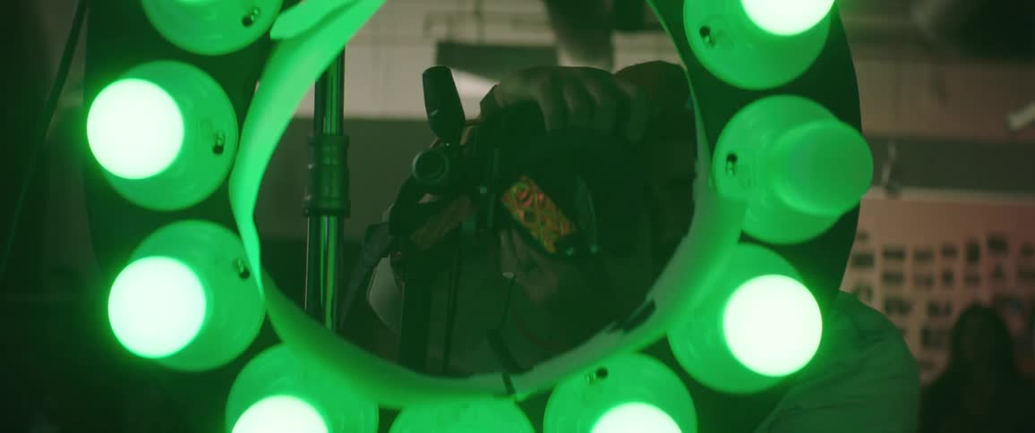 A man with a hat taking pictures with a camera with people and a wall in the background