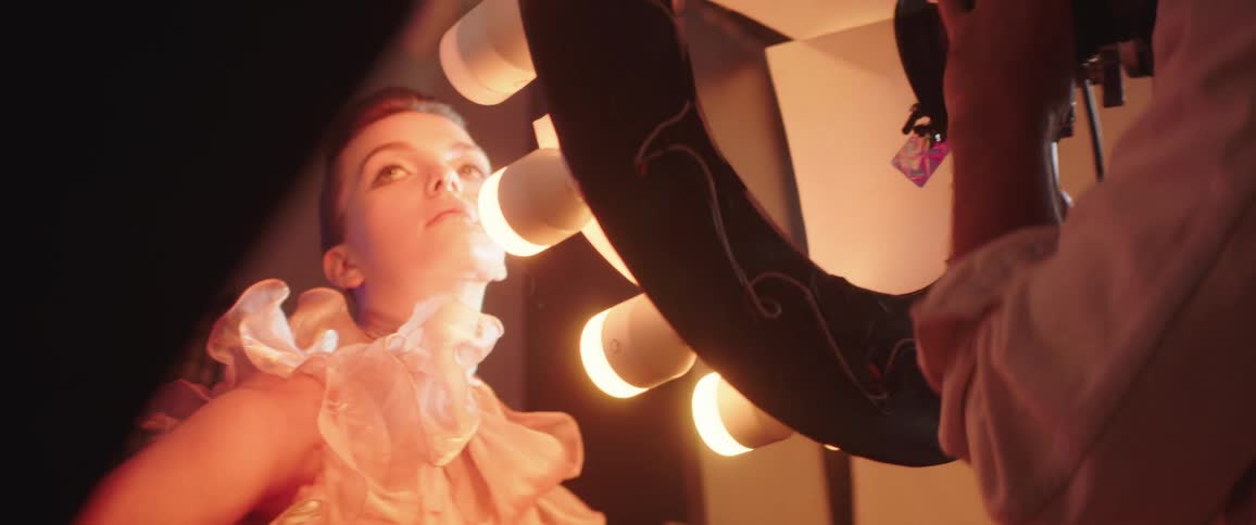 A woman poses in front of large colored lights for a photographer