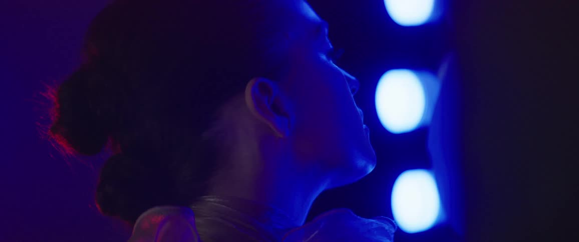 Woman looks up then tilts her head downwards as lights flash around her
