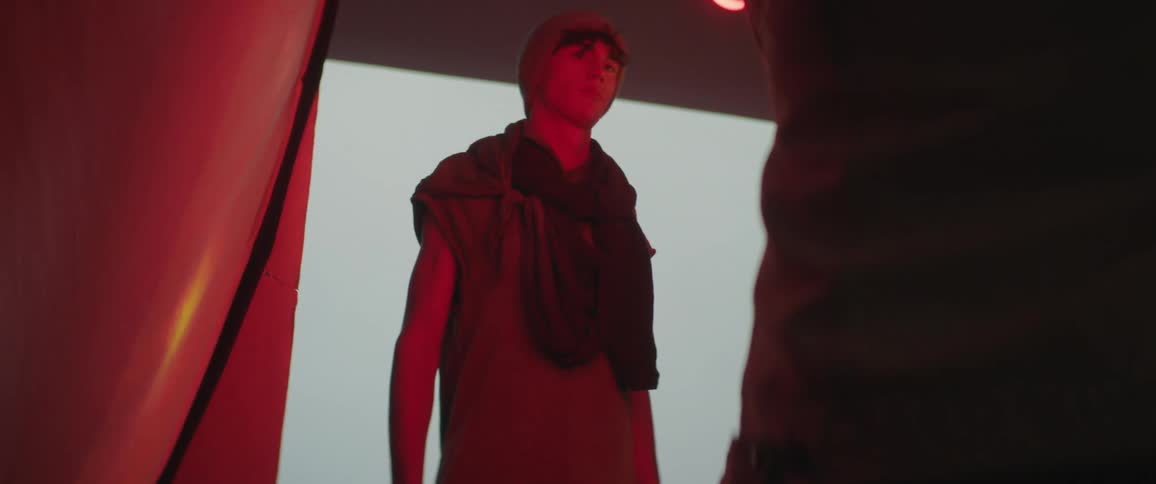 Male fashion model poses in front of large screen of changing images under colored lighting as camera flashes