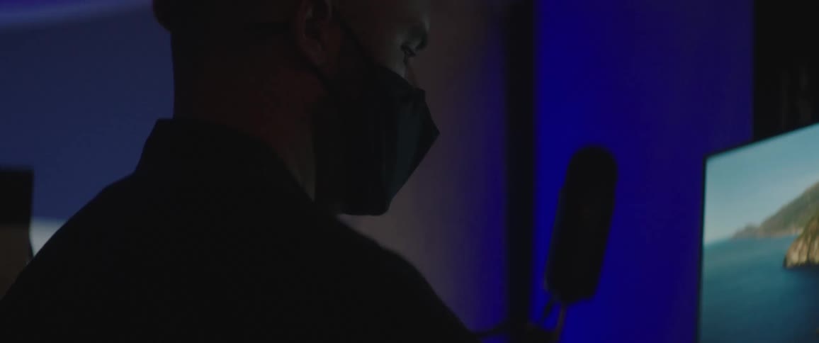 Photographer wearing face mask works with images on screen in room tinted by colored lights