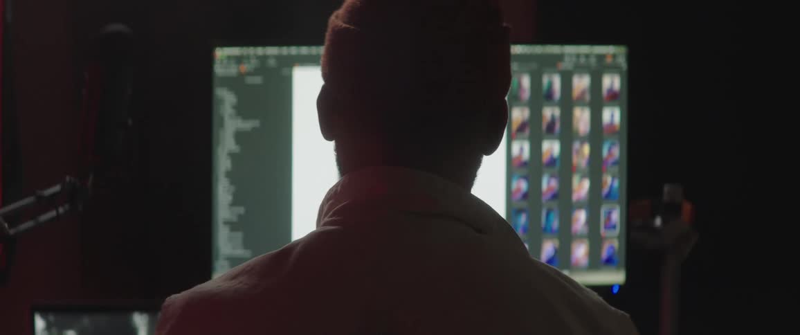 A man with a hat in a room with computer screens and a microphone