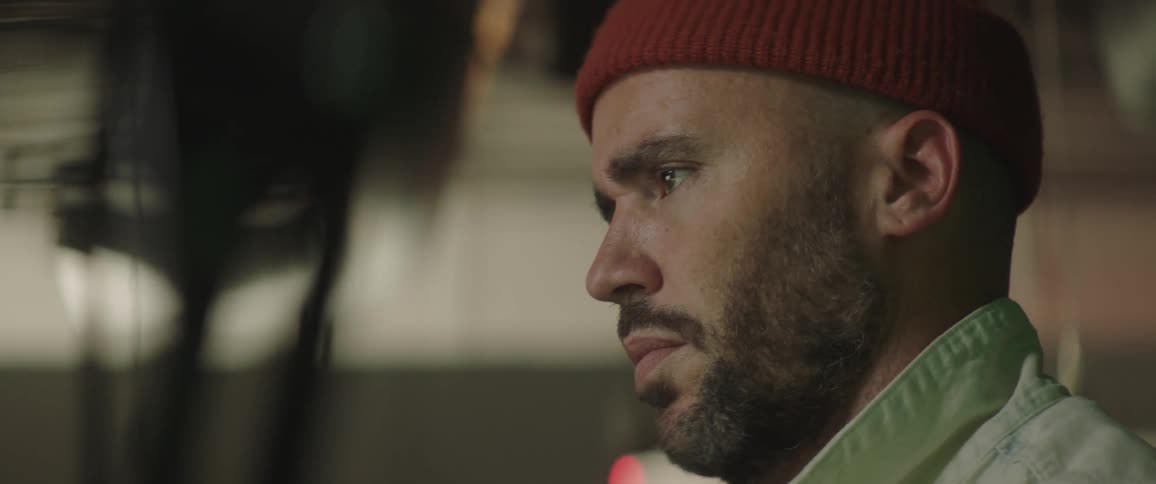 Man with a beard a red woolly hat a white jacket uses desktop talking in the art studio