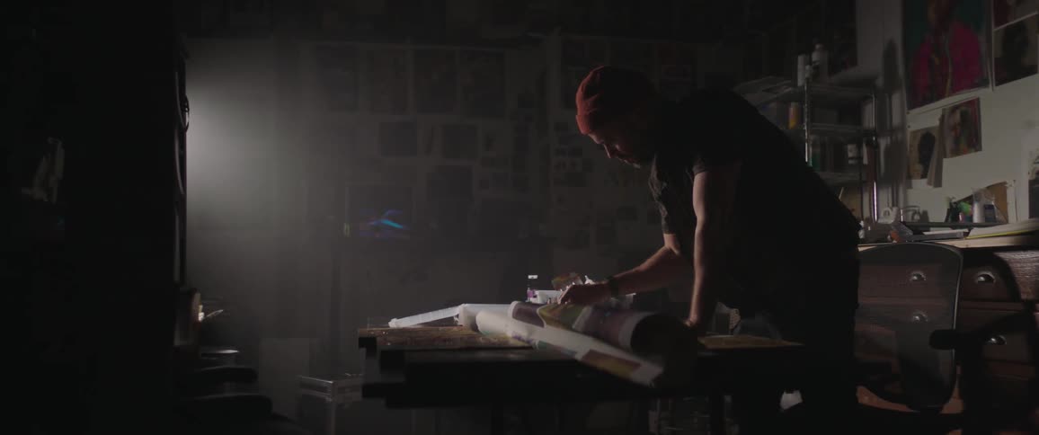 A man in a room applying paint to a canvas on a table