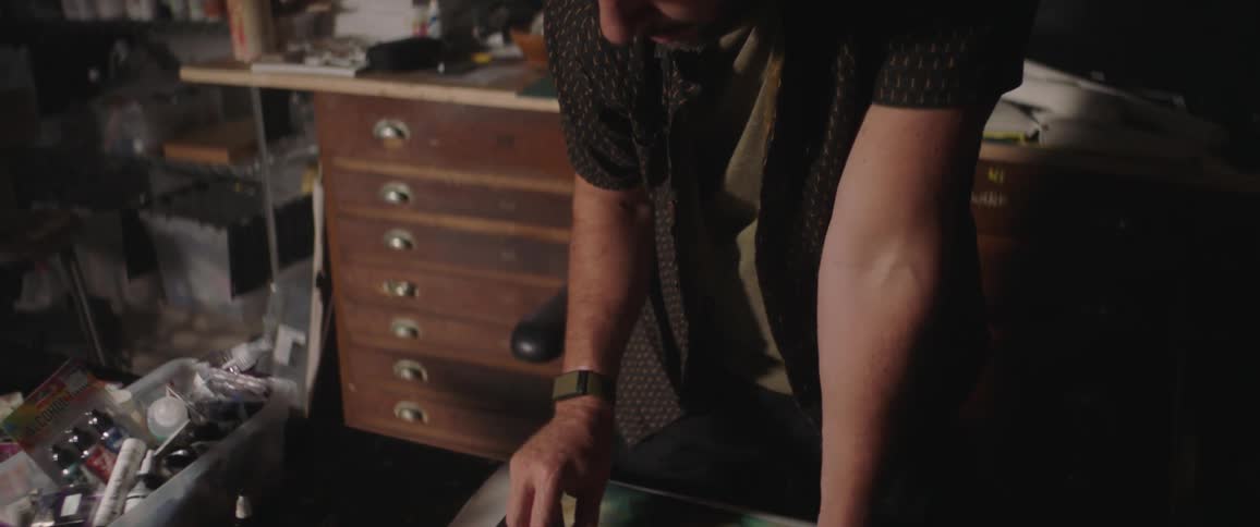A man is standing in a cluttered room and is painting