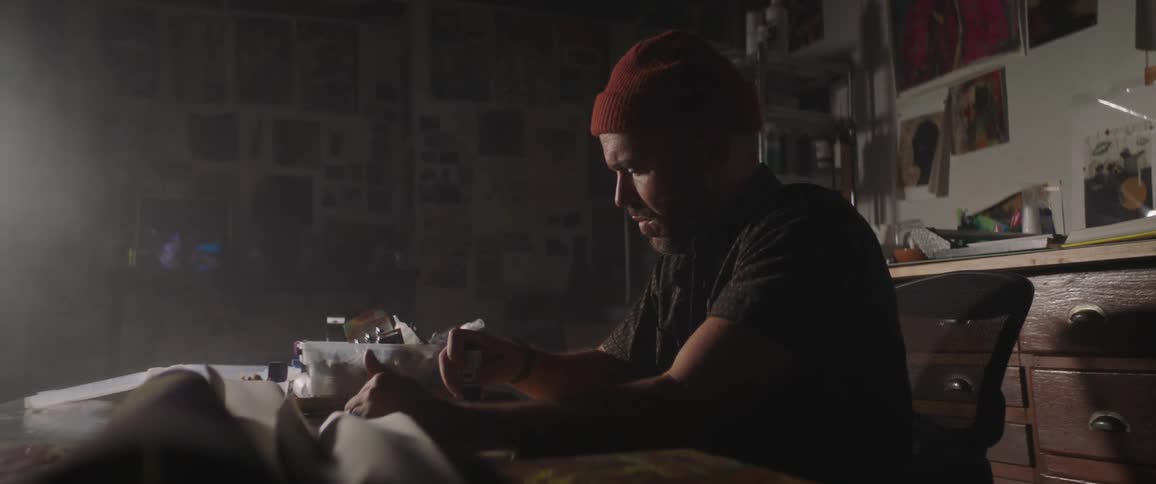 Male painter with red beanie a beard and a dark shirt paints on canvas in the art studio