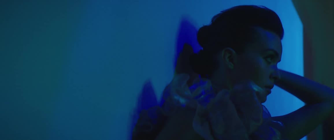 Fashion model wearing ruffled outfit poses against wall under changing colored lights as camera flashes