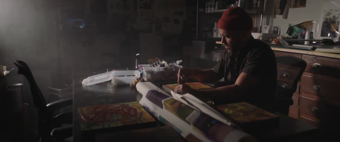 Man sits at table in art studio applying paint to canvas