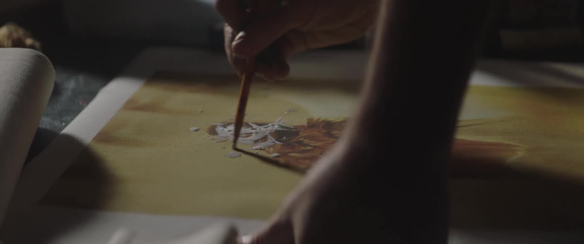 A person in a room smearing paint with a pencil on a canvas