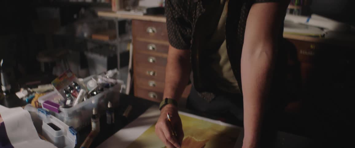 A man leans over a table and paints on a piece of a paper