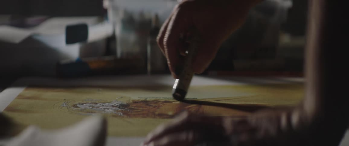 A person in a room applying paint to a canvas on a table