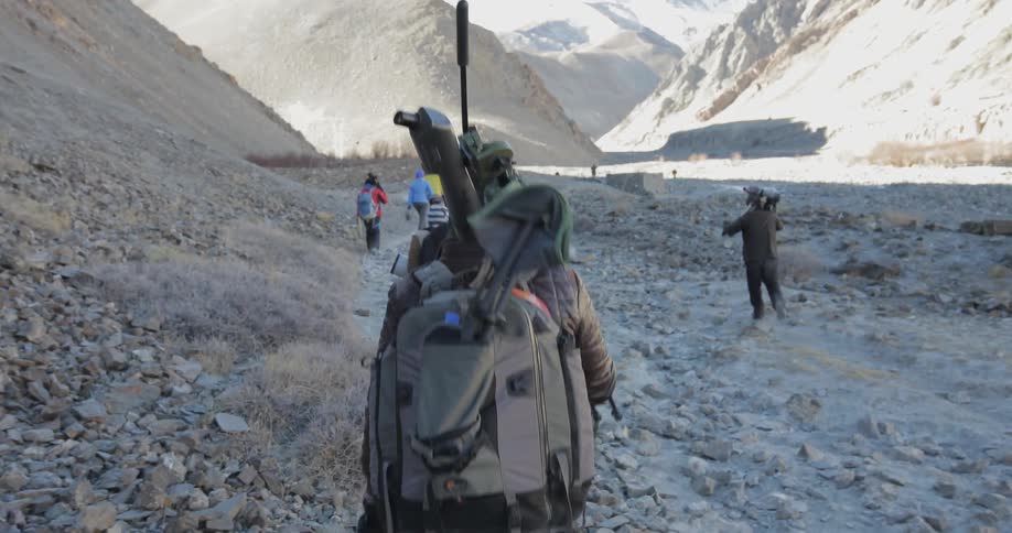 Group of people walk over rocky terrain towards mountains
