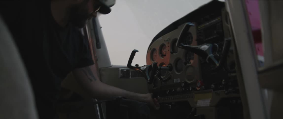 A man with a hat and sunglasses in a aircraft cockpit touching buttons