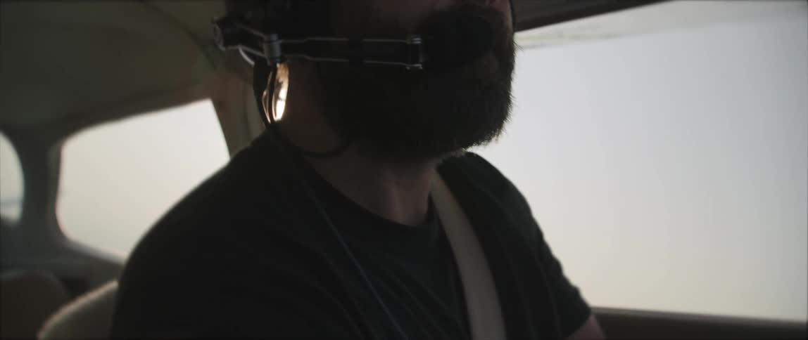 A man with a headset and sunglasses flying an aircraft with the sky and clouds in the background