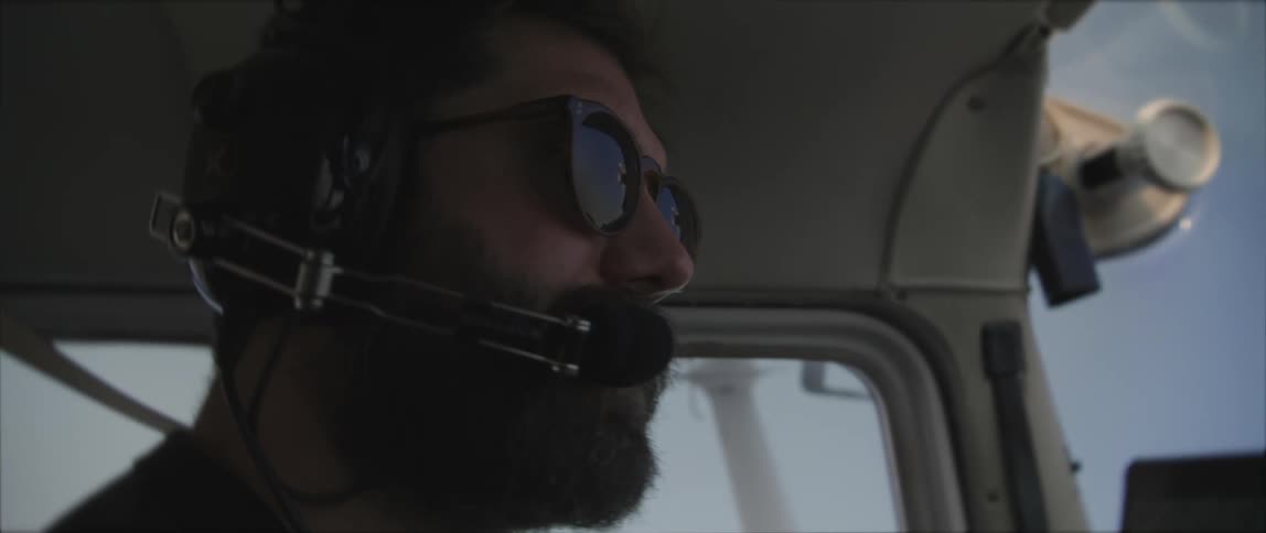 Pilot wearing headset sits in cockpit under clear blue sky