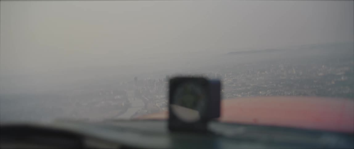 Fog shrouded river and city show through window cockpit of propeller plane