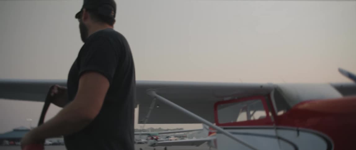 A man removes a bag from the propeller of a small plane at an airfield
